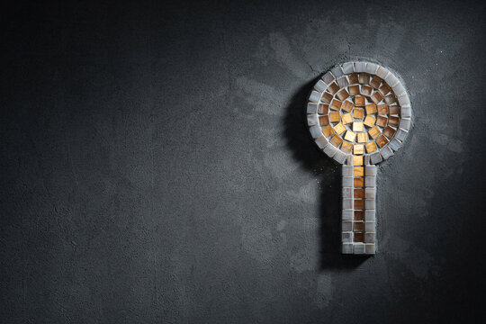 Key symbol made of amber and pearl mosaic tiles on a grey textured wall