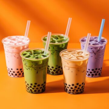 Assorted colorful bubble tea drinks in clear plastic cups with dark tapioca pearls served on a vibrant orange background for summer menus, cold, drink, tea