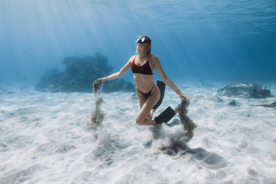 Female free diver swimming underwater with sand in hands