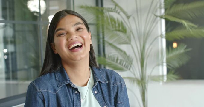 African American woman smiling and laughing, responding to off camera joke in office wearing denim
