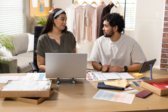 African American partners discussing clothing sketches and swatches at home studio with laptop
