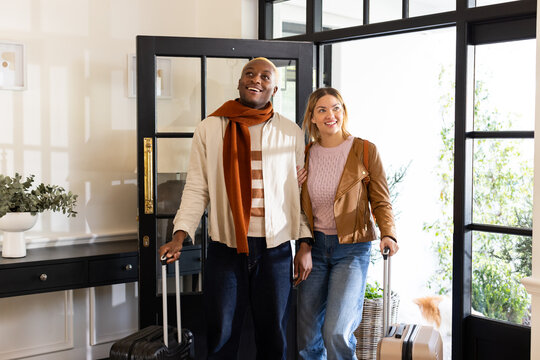 African American couple standing in bright home foyer holding rolling suitcases and linking arms