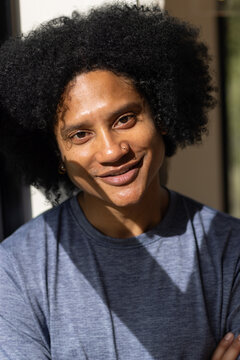 Adult African American man smiling and tilting head, wearing grey tee, showing nose hoop