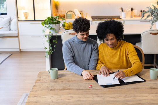 Two African American men sitting at wooden kitchen table signing papers in black portfolio with pen