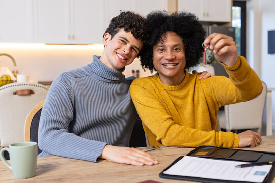 Two African American men wearing sweaters sitting in modern kitchen at wooden table
