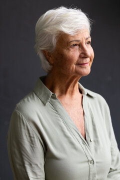 Senior female posing in studio, gazing right, wearing sage-green button-up blouse, short white hair