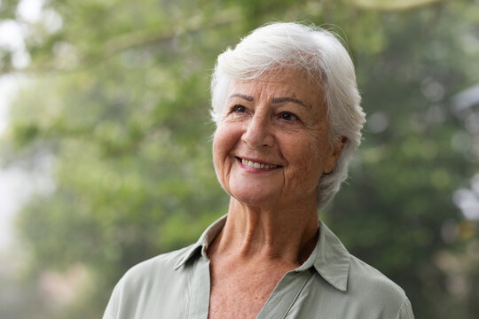 Senior female standing in park, short white hair wearing sage collared shirt smiling, gazing right
