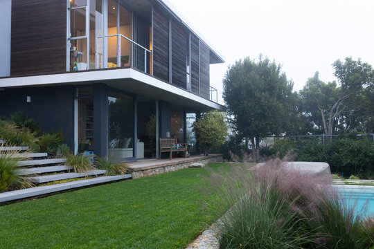 Modern two-story house is featuring glass balcony, sliding doors to deck, pool with purple grasses