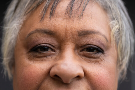 Senior African American female facing camera, showing textured skin, eyeliner and makeup in studio