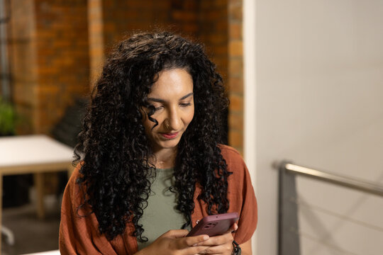 African American woman standing in office with rust cardigan holding pink phone checking wristwatch
