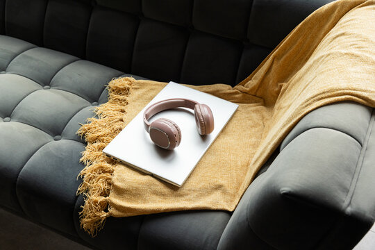 Rose-gold wireless headphones are resting on white laptop on mustard throw on tufted grey sofa