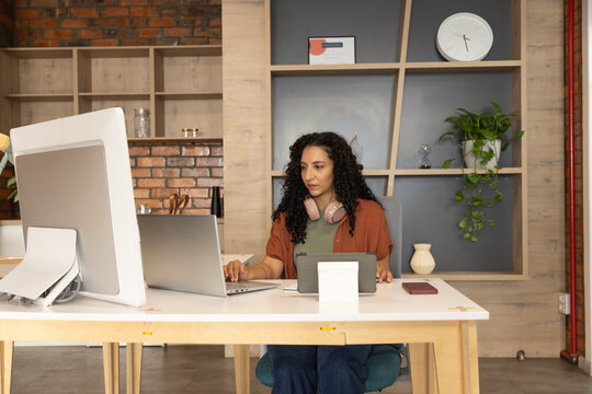 African American woman working on laptop at modern office using external monitor and headphones