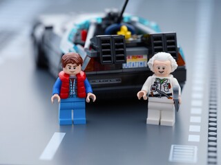 Fototapeta premium Tambov, Russian Federation - June 20, 2026 Lego minifigures of Marty McFly and Doc Brown standing near the back of DeLorean time machine car from Back to the Future on a road baseplate.