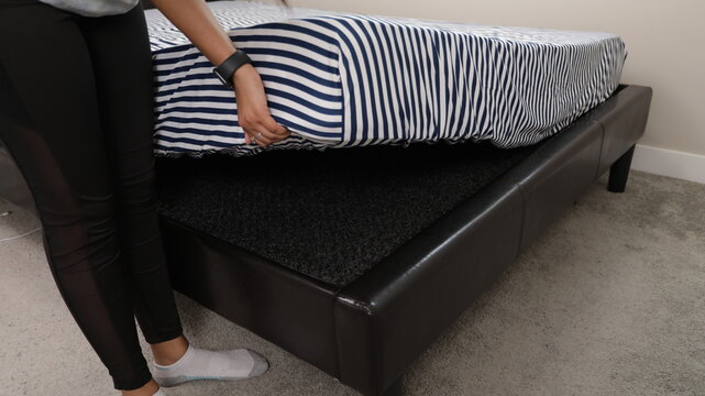 Woman lifting a striped mattress to reveal a black breathable mesh underlay showing mattress ventilation airflow moisture control bed protection easy installation and bedroom comfort