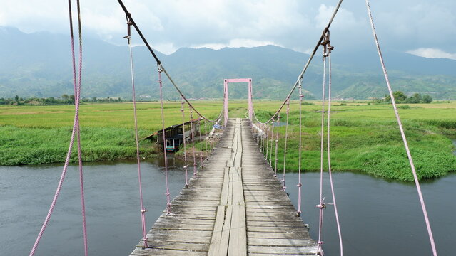 Suspension bridge crossing Rawa Bento wetlands surrounded by rice fields and mountain landscape