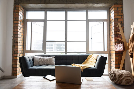 Dark grey tufted sofa is occupying center space in loft, in front of large grid window
