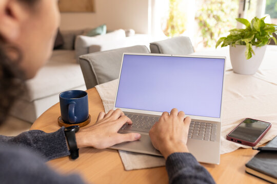 African American man typing on silver laptop at round wooden table with blue mug wearing smartwatch