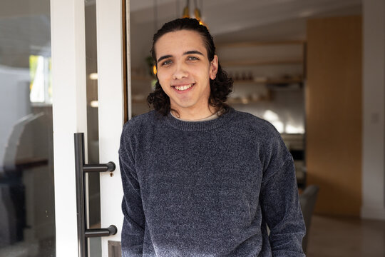 Adult male standing at glass door at home, leaning on black pull handle, wearing gray sweater