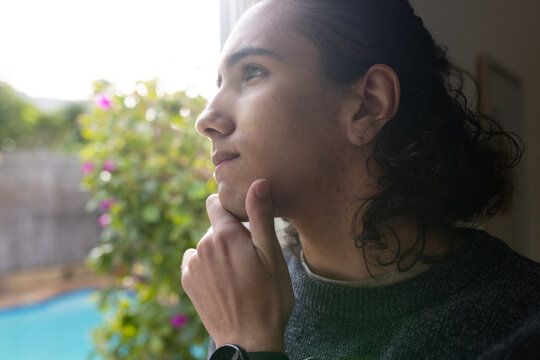 Male looking out large window at home, resting chin on hand, wearing smartwatch, copy space