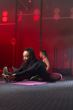 Female partners stretching on purple mats at gym rig with rings wearing leggings and watch