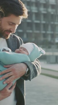 Dad gently kisses sleeping newborn outside, Gentle father embracing and kissing infant during sunny day in city park