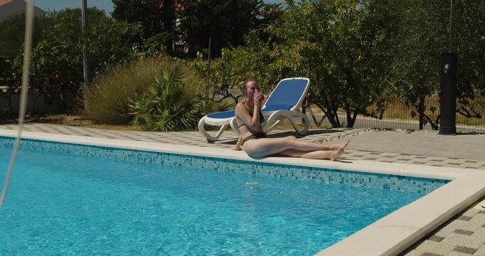 Young woman relaxing by a swimming pool and enjoying a refreshing drink on a sunny summer day, representing vacation, leisure, relaxation and outdoor lifestyle.