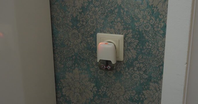Close-up of a hand plugging an electric mosquito repellent device into a wall socket at home, representing insect protection, pest control and mosquito prevention.