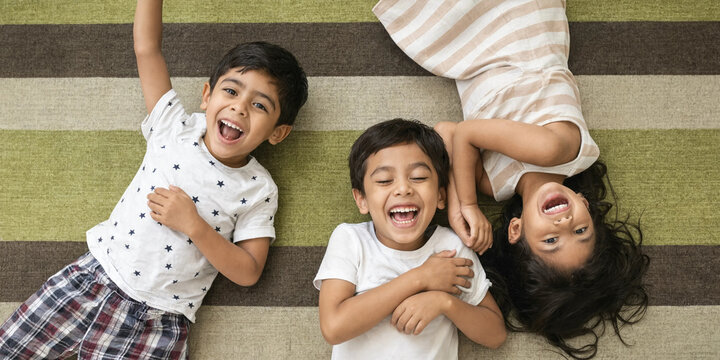 Siblings playing and laughing while lying on a colorful rug  