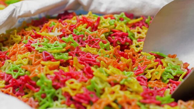Vibrant assorted gummy candies in red, yellow, green, orange colors arranged in white paper box or tray for retail display.