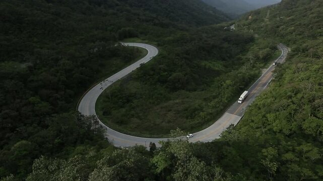 Drone acompanha rodovia c&ecirc;nica em zigue-zague na montanha cercada por mata verdejante.