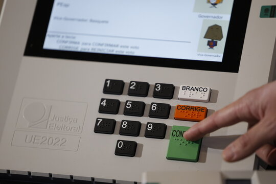 Close-up of a Brazilian voter pressing a button on an electronic voting machine at a polling station during the 2026 Brazilian elections, illustrating electronic voting, democracy, civic participation