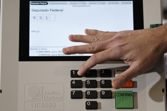 Close-up of a Brazilian voter pressing a button on an electronic voting machine at a polling station during the 2026 Brazilian elections, illustrating electronic voting, democracy, civic participation