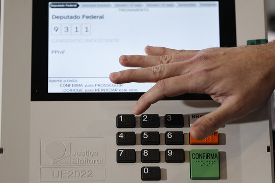 Close-up of a Brazilian voter pressing a button on an electronic voting machine at a polling station during the 2026 Brazilian elections, illustrating electronic voting, democracy, civic participation