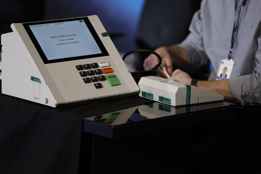 Close-up of a Brazilian voter pressing a button on an electronic voting machine at a polling station during the 2026 Brazilian elections, illustrating electronic voting, democracy, civic participation