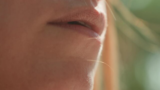 Woman applies lip gloss focusing on close up details of her lips and hand movements. scene emphasizes texture detail under soft lighting with natural background