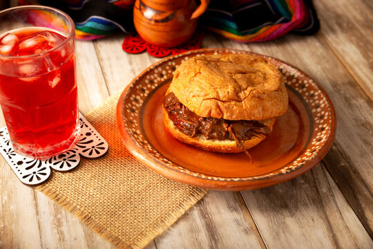 Mexican hojaldra with mole on a rustic clay plate, served with hibiscus water in a traditional setting. Homemade mexican food.
