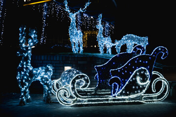 Glowing Santa sleigh and reindeer light sculptures in outdoor Christmas decoration at night, festive winter illumination and holiday display. © svetlana_cherruty
