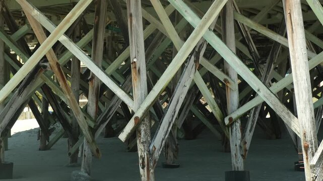 Wooden supports of a beach pier show their structure during midday hours in a coastal location