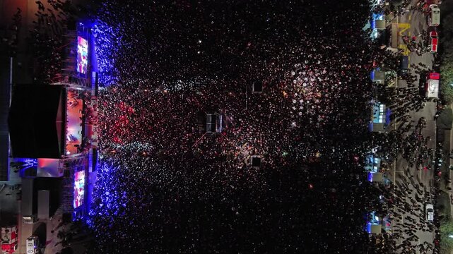 Aerial top view of crowd at night music concert. People gathered at festival outdoor stage with lights and screens, 4k