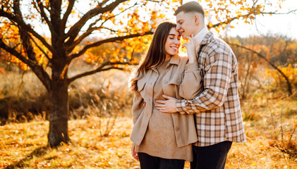 Naklejka premium Young couple on date in autumn forest enjoys relaxing time at sunset. Man and woman embrace and spend time together. Concept of leisure and love. Autumn day.