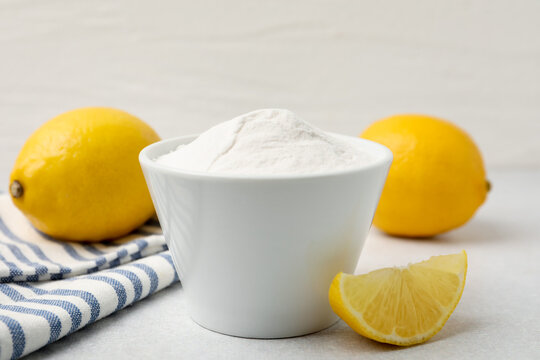 Baking soda in bowl and lemons on light grey table, closeup