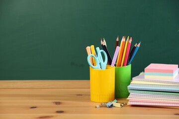 Different stationery on wooden table near chalkboard. Space for text © New Africa