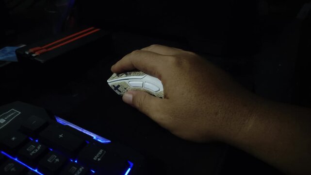 Closeup Hand using a gaming mouse beside an RGB keyboard in a dark computer setup.
