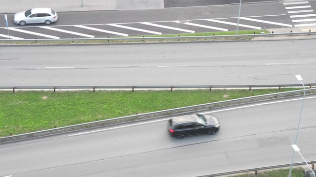 Passenger cars travel along divided urban road lanes beside a slip road and pedestrian crossing, illustrating traffic circulation and transport infrastructure