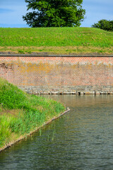 Obraz premium Grassy moat shoreline with historic brick fortification wall.