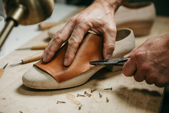Shoemaker stretching tan leather over a wooden shoe last with lasting pliers