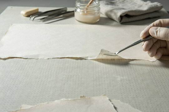Conservator lifting a repair patch on a torn sheet of old paper with fine tools nearby