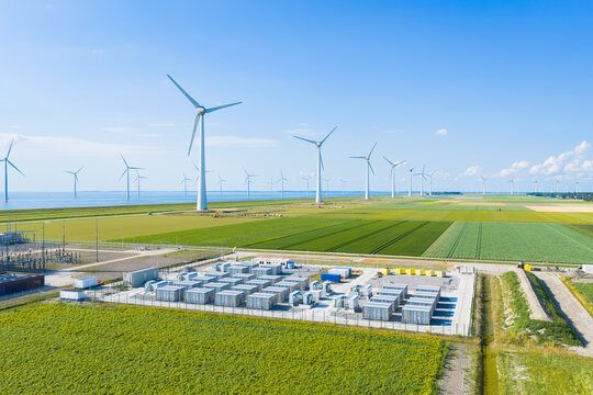 Aerial view of battery energy storage system facility next to wind turbines. Industrial lithium battery system for renewable power plant and grid management.