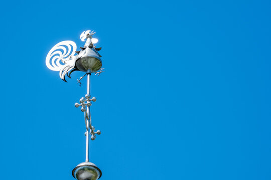 metal rooster weather vane mounted atop pole against blue sky, Classic weathervane, directional arrows, rural architecture wind measurement and decorative rooftop elements in European villages