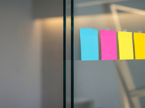 Blank colorful sticky notes attached to a glass wall in a modern office for brainstorming and planning